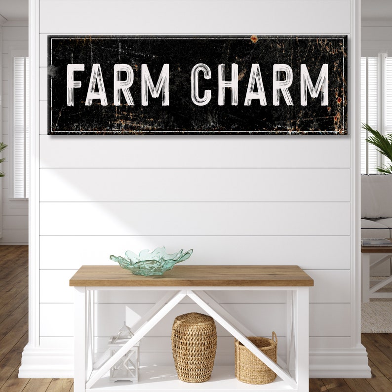 Puede incluir: Un letrero en blanco y negro con el texto "FARM CHARM" en una fuente desgastada. El letrero est&aacute; colgado en una pared blanca de tablones de madera sobre una mesa de madera con un cuenco de vidrio y dos cestas tejidas.