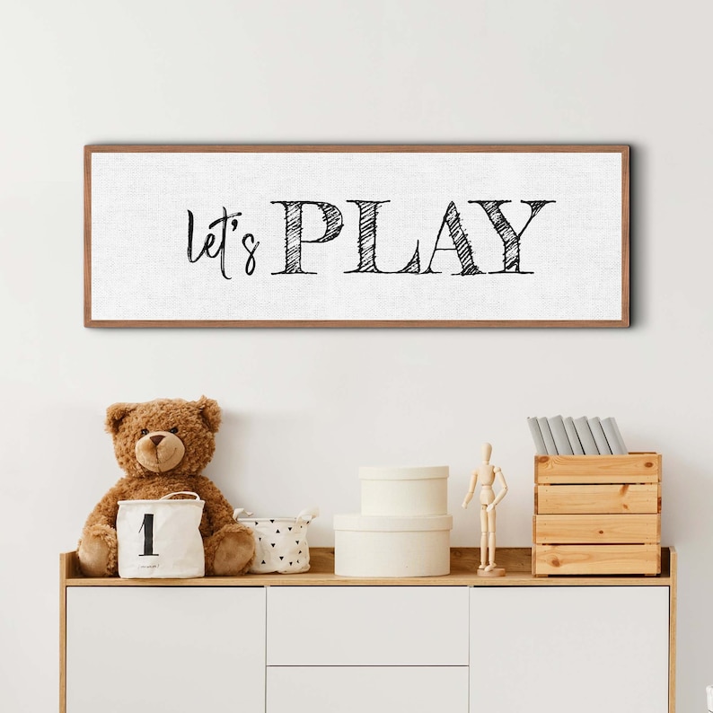 May include: A wooden framed canvas sign with the text "Let's Play" in black script font on a white background.