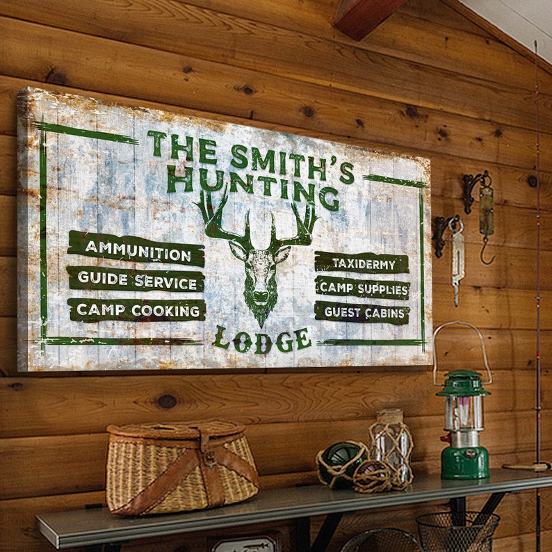 May include: A rustic wooden sign with the text "The Smith's Hunting Lodge" in green letters. The sign features a green silhouette of a deer with antlers and a list of services offered: Ammunition, Guide Service, Camp Cooking, Taxidermy, Camp Supplies, and Guest Cabins.