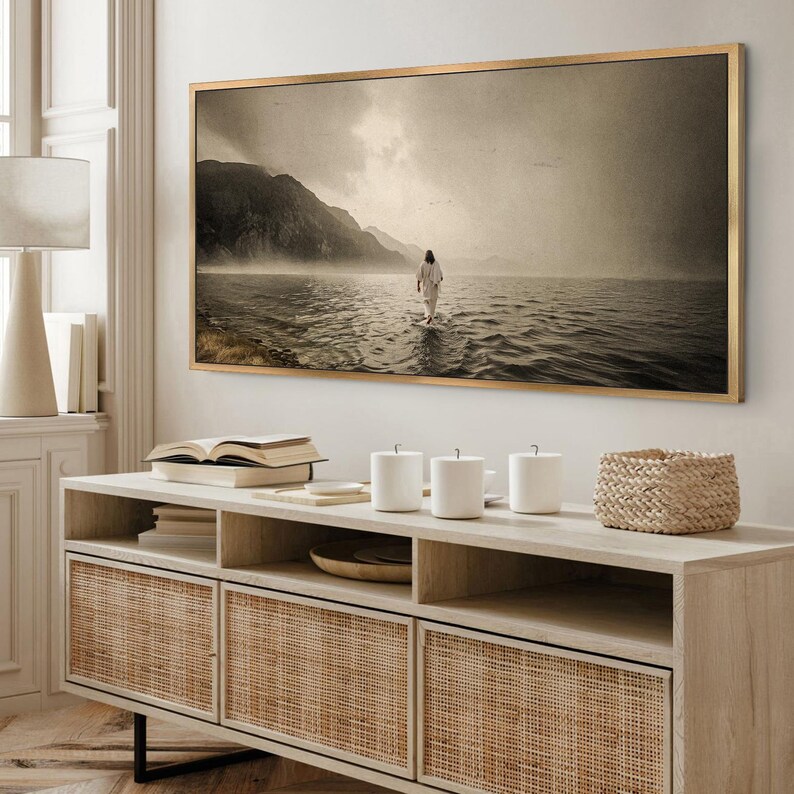 Pu&ograve; includere: Una stampa in tonalit&agrave; seppia incorniciata raffigura una persona che cammina sull'acqua verso le montagne sotto un cielo nuvoloso. L'opera d'arte &egrave; appesa sopra un mobile in legno chiaro con ante in rattan intrecciato. Sono visibili anche tazze bianche e un cestino intrecciato.