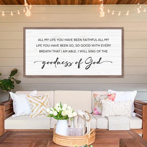 Puede incluir: Un letrero de madera enmarcado con el texto "ALL MY LIFE YOU HAVE BEEN FAITHFUL ALL MY LIFE YOU HAVE BEEN SO, SO GOOD WITH EVERY BREATH THAT I AM ABLE. I WILL SING OF THE goodness of God" en escritura negra. El letrero est&aacute; sobre un sof&aacute;.
