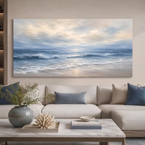 May include: A rectangular landscape oil painting featuring a serene ocean scene with gentle waves rolling onto a sandy shore under a soft, cloudy sky. The colour palette consists of muted blues, whites, and warm beige tones with visible brushstrokes.