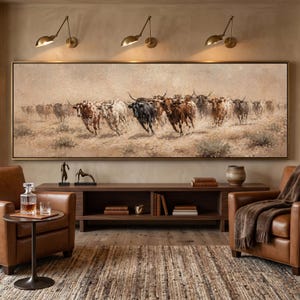 May include: A large horizontal framed oil painting depicting a herd of longhorn cattle running across a dusty, beige landscape. The artwork features various shades of brown, tan, and black, capturing the movement of the animals in a wide, panoramic view.