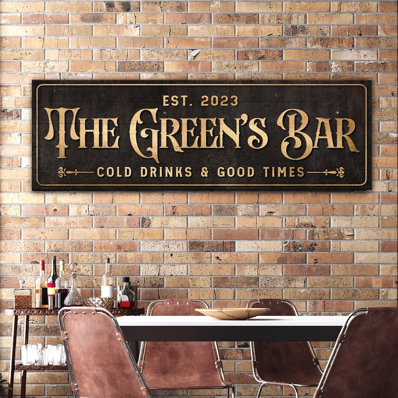 K&ouml;nnte beinhalten: Ein schwarzes Holzschild mit goldenen Buchstaben, auf dem "The Green's Bar Est. 2023 Cold Drinks & Good Times" steht. Das Schild h&auml;ngt an einer Backsteinwand.
