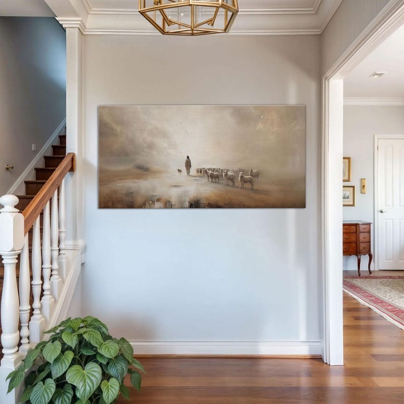 Puede incluir: Una pintura de paisaje rectangular representa a un pastor con un perro y un reba&ntilde;o de ovejas en una escena brumosa en tonos sepia. La obra de arte cuelga de una pared gris claro en un pasillo con una escalera y una planta de interior.