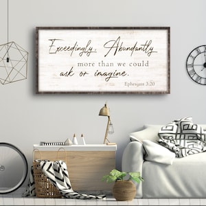 May include: A rectangular wall sign with a distressed white background and a dark brown frame. The sign features dark brown cursive and serif text that reads: Exceedingly, Abundantly more than we could ask or imagine. Ephesians 3:20.