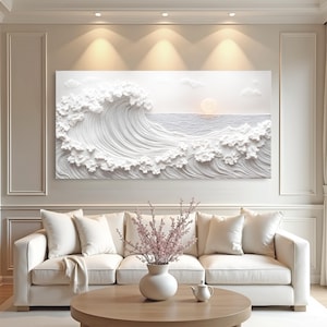 May include: A large, white, 3D relief artwork depicting a crashing ocean wave with a setting sun. The artwork is mounted above a white sofa with cream-colored pillows. A round, light brown coffee table and a vase of pink flowers are in front of the sofa.