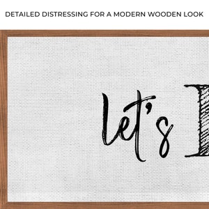 May include: A white canvas sign with a brown wooden frame. The sign has black handwritten text that says "Let's" in a cursive font.