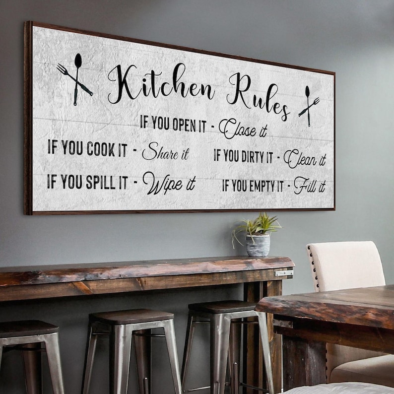 A Farmhouse Kitchen canvas sign with Kitchen rules on it on a distressed white wooden-inspired background.