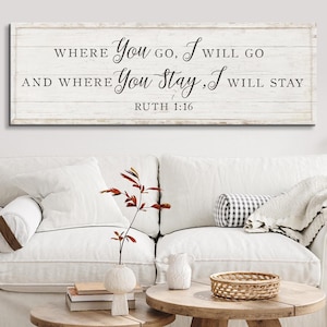 K&ouml;nnte beinhalten: Ein rechteckiges Holzschild mit dem Text "WHERE YOU GO, I WILL GO AND WHERE YOU STAY, I WILL STAY RUTH 1:16" in schwarzer Schrift. Das Schild ist &uuml;ber einem wei&szlig;en Sofa mit dekorativen Kissen und einem Holztisch angebracht.