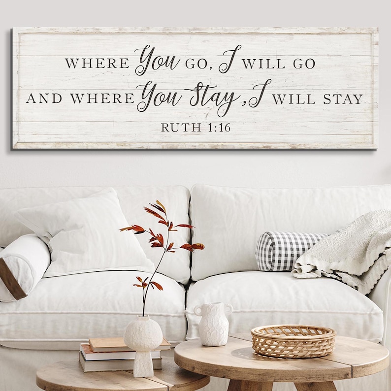 K&ouml;nnte beinhalten: Ein rechteckiges Holzschild mit dem Text "WHERE YOU GO, I WILL GO AND WHERE YOU STAY, I WILL STAY RUTH 1:16" in schwarzer Schrift. Das Schild ist &uuml;ber einem wei&szlig;en Sofa mit dekorativen Kissen und einem Holztisch angebracht.