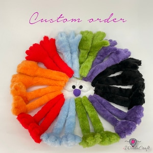 May include: A circular arrangement of fuzzy, plush limbs in red, orange, light blue, green, purple, and black, surrounding a central white face with two black eyes and a purple nose. The text Custom order is written in pink at the top.