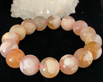 May include: A pink and white agate gemstone bracelet with a pink elastic cord. The beads are round and have a natural, polished finish.