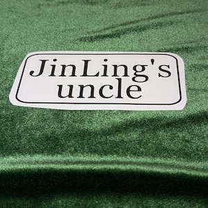 May include: White rectangular label with black text that reads "JinLing's uncle" on a green fabric background.