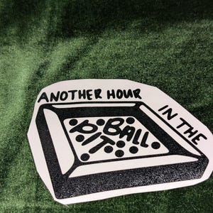 May include: A white sticker with black text and a pool table graphic. The text reads "ANOTHER HOUR IN THE POOL PIT". The sticker is on a green velvet background.