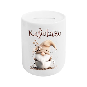 Könnte beinhalten: Weiße Keramik-Spardose mit einem Schlitz oben, mit einem skurrilen Zwerg-Design. Der Zwerg trägt eine Strickmütze und sitzt in einer Kaffeetasse, umgeben von Kaffeebohnen und floralen Akzenten. Über dem Zwerg steht das Wort "Kaffeekasse".