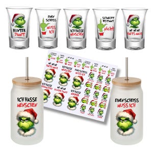 Könnte beinhalten: Eine Sammlung von Grinch-Themen-Trinkgläsern und Aufklebern. Enthält Schnapsgläser und Glasbecher mit Bambusdeckeln. Die Schnapsgläser und Becher zeigen den Grinch mit Weihnachtsmütze und verschiedenen deutschen Sätzen.