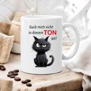 Könnte beinhalten: Weiße Keramiktasse mit einer schwarzen Katzendarstellung und dem Text "Guck mich nicht in diesem TON an!"