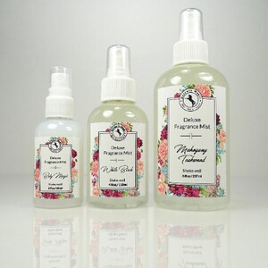 May include: Three glass bottles of fragrance mist with white spray tops and floral labels. The bottles are labeled "Deluxe Fragrance Mist" with the scents "Baby Magic", "White Birch", and "Mahogany Teakwood".