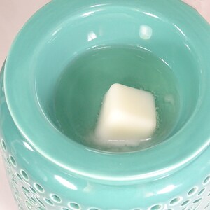 Może przedstawiać: Tealowy ceramiczny podgrzewacz do wosku z białą wkładką woskową w środku. Podgrzewacz ma ozdobny wz&oacute;r z małych k&oacute;łek.