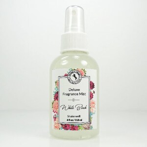 May include: A clear glass bottle with a white spray top and a white label. The label has a floral design and the text "Deluxe Fragrance Mist - White Birch - Shake well 4 fl oz/118 ml".