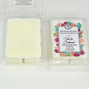 Może przedstawiać: Biały wosk wtopiony w przezroczysty plastikowy pojemnik z etykietą o kwiatowym wzorze. Etykieta zawiera napis "100% Pure Soy Wax ręcznie wlewany z delikatnym zapachem" i "Teak & Oudwood Deluxe Wax Melt 2.7 oz/77g".