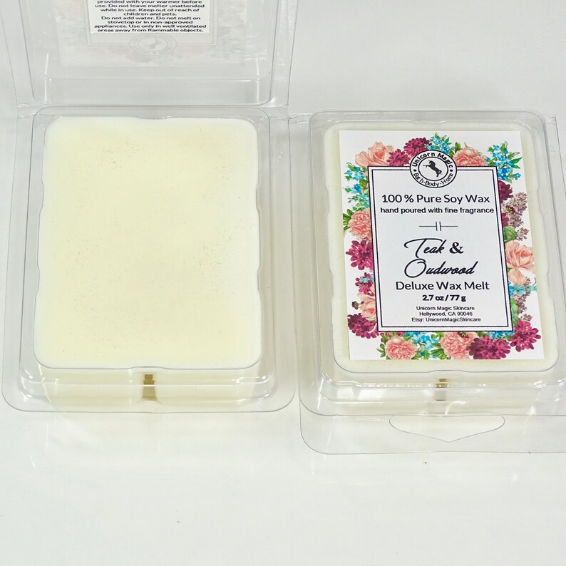 Może przedstawiać: Biały wosk wtopiony w przezroczysty plastikowy pojemnik z etykietą o kwiatowym wzorze. Etykieta zawiera napis "100% Pure Soy Wax ręcznie wlewany z delikatnym zapachem" i "Teak & Oudwood Deluxe Wax Melt 2.7 oz/77g".