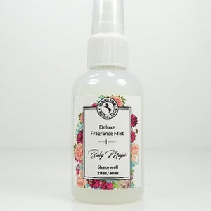 May include: A clear plastic bottle with a white pump top and a white label. The label has a floral design and the text "Deluxe Fragrance Mist - Baby Magic - Shake well 2 fl oz/60 ml".