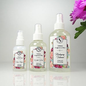 May include: Three glass bottles of fragrance mist with white labels and floral designs. The bottles are labeled "Deluxe Fragrance Mist" and have different scents: "Baby Magic", "White Birch", and "Mahogany Teakwood".