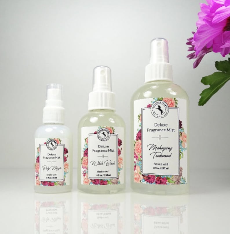 May include: Three glass bottles of fragrance mist with white labels and floral designs. The bottles are labeled "Deluxe Fragrance Mist" and have different scents: "Baby Magic", "White Birch", and "Mahogany Teakwood".