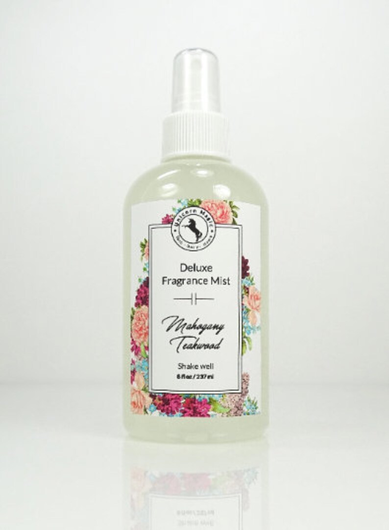 May include: A clear glass bottle with a white spray top and a white label. The label has a floral design and the text "Deluxe Fragrance Mist Mahogany Teakwood Shake well 8 fl oz/237 ml".