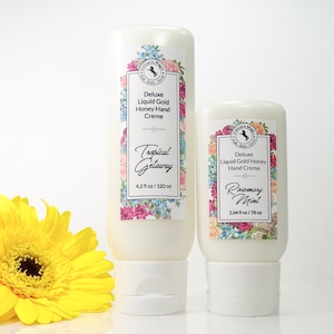 May include: Two white plastic bottles of hand cream with floral labels. The larger bottle is labeled "Tropical Getaway" and is 4.2 fluid ounces. The smaller bottle is labeled "Rosemary Mint" and is 2.64 fluid ounces.