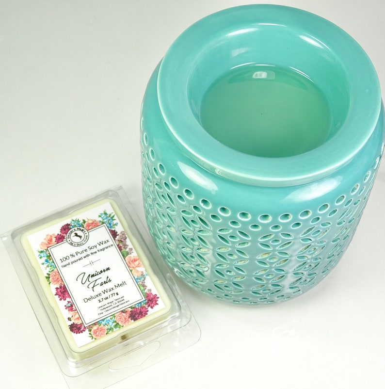 Może przedstawiać: Tealowy ceramiczny podgrzewacz do wosku z ozdobnym wzorem wyciętym. W zestawie znajduje się mały biały wosk do topienia, oznaczony jako "Unicorn Farts" i "Deluxe Wax Melt 2.7 oz/77g".