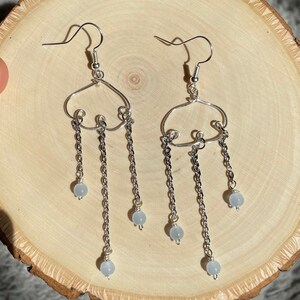 May include: Silver dangle earrings with a cloud-shaped design and three chains with light blue beads hanging from each chain.