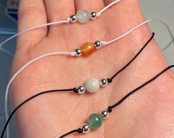 Puede incluir: Tres collares simples con piedras de diferentes colores y cuentas plateadas. Los collares están sobre un fondo blanco.