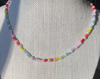 May include: A rainbow beaded necklace with white pearl beads. The necklace is on a white mannequin.