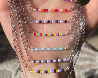 May include: A set of seven layered necklaces with silver chains and colorful beaded bars. Each bar features a different color combination of small, round beads.