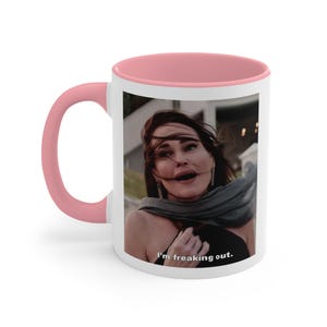 Op de afbeelding: Witte keramische koffiemok met een roze rand. De mok heeft een foto van een vrouw met wapperend haar en de tekst "I'm freaking out."