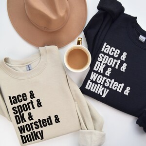 Op de afbeelding: Twee sweatshirts met de tekst "lace & sport & DK & worsted & bulky" erop gedrukt. E&eacute;n sweatshirt is beige en de andere is zwart.