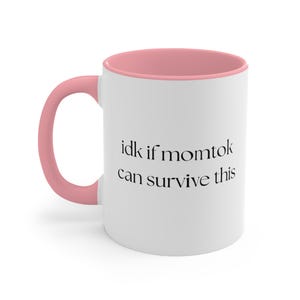 Op de afbeelding: Witte keramische mok met een roze binnenkant en oor. De mok heeft de tekst "idk if momtok can survive this" in zwart, gecentreerd op de voorkant. De mok is ontworpen voor warme of koude dranken.