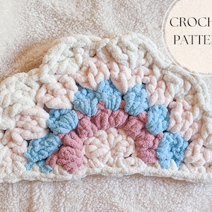 May include: A crochet cloud pattern with a rainbow of colors, including white, pink, and blue. The pattern is made with chunky yarn and has a fluffy texture.