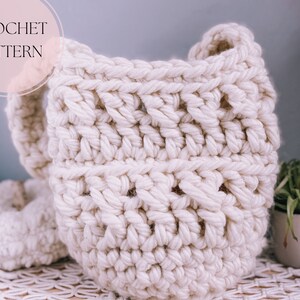 May include: A white crocheted tote bag with a crocheted handle. The bag is made with a chunky yarn and has a textured stitch pattern.