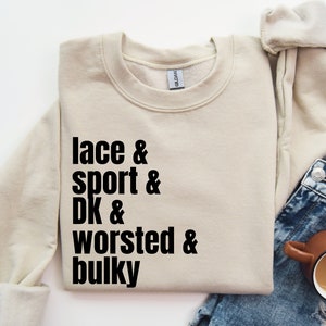 Op de afbeelding: Een beige sweatshirt met de tekst "lace & sport & DK & worsted & bulky" in het zwart gedrukt.