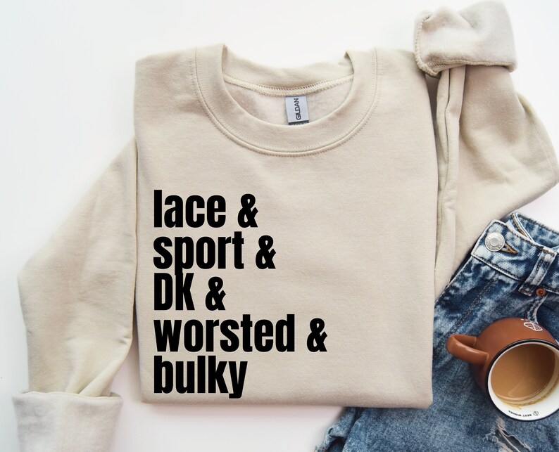 Op de afbeelding: Een beige sweatshirt met de tekst "lace & sport & DK & worsted & bulky" in het zwart gedrukt.