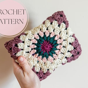 Puede incluir: Un proyecto de granny square tejido a ganchillo de forma rectangular, con una paleta de colores crema, rosa, verde azulado y magenta intenso. El texto "CROCHET PATTERN" se muestra en un círculo rosa. El proyecto se sostiene en una mano.