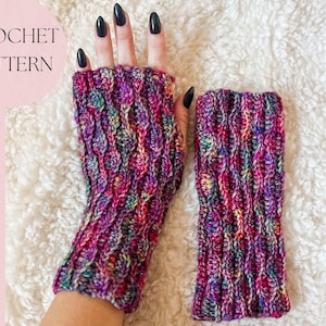 May include: A pair of colorful crocheted fingerless gloves with a cable stitch pattern. The gloves are made with a multi-colored yarn in shades of pink, purple, and blue. CROCHET PATTERN is written in white text on a pink background.