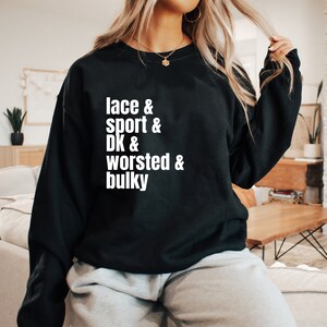Op de afbeelding: Zwart sweatshirt met witte tekst die "lace & sport & DK & worsted & bulky" zegt