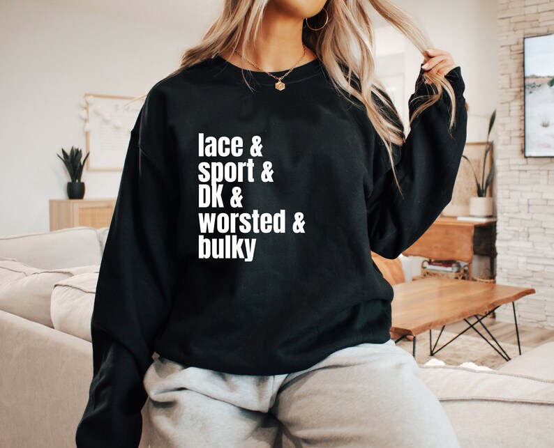 Op de afbeelding: Zwart sweatshirt met witte tekst die "lace & sport & DK & worsted & bulky" zegt