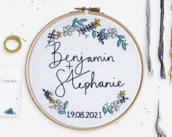May include: A white embroidery hoop with a floral wreath design, the names "Benjamin + Stephanie" and the date "19.08.2021".