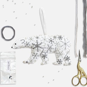 May include: A white felt polar bear ornament with a snowflake design, a small bag of beads, embroidery floss, and gold embroidery scissors.
